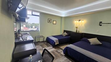 A hotel room with two beds, a desk with a gas stove, a chair, and a small table with a bottle and remote control.