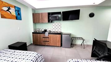 A compact room with two beds, a kitchenette, a flat-screen TV, and a clock on the wall.