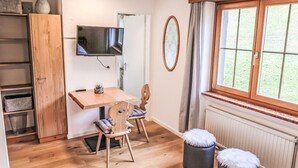 A cozy room with a wooden table, a TV mounted on the wall, a window with curtains, and a radiator. - La Siala Apt.21 by Interhome (Falera)
