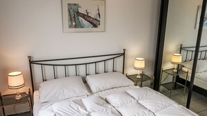 Ein ordentlich bezogenes Bett mit weißer Bettwäsche, zwei Nachttischlampen, ein gerahmtes Bild an der Wand und ein großer Spiegel.