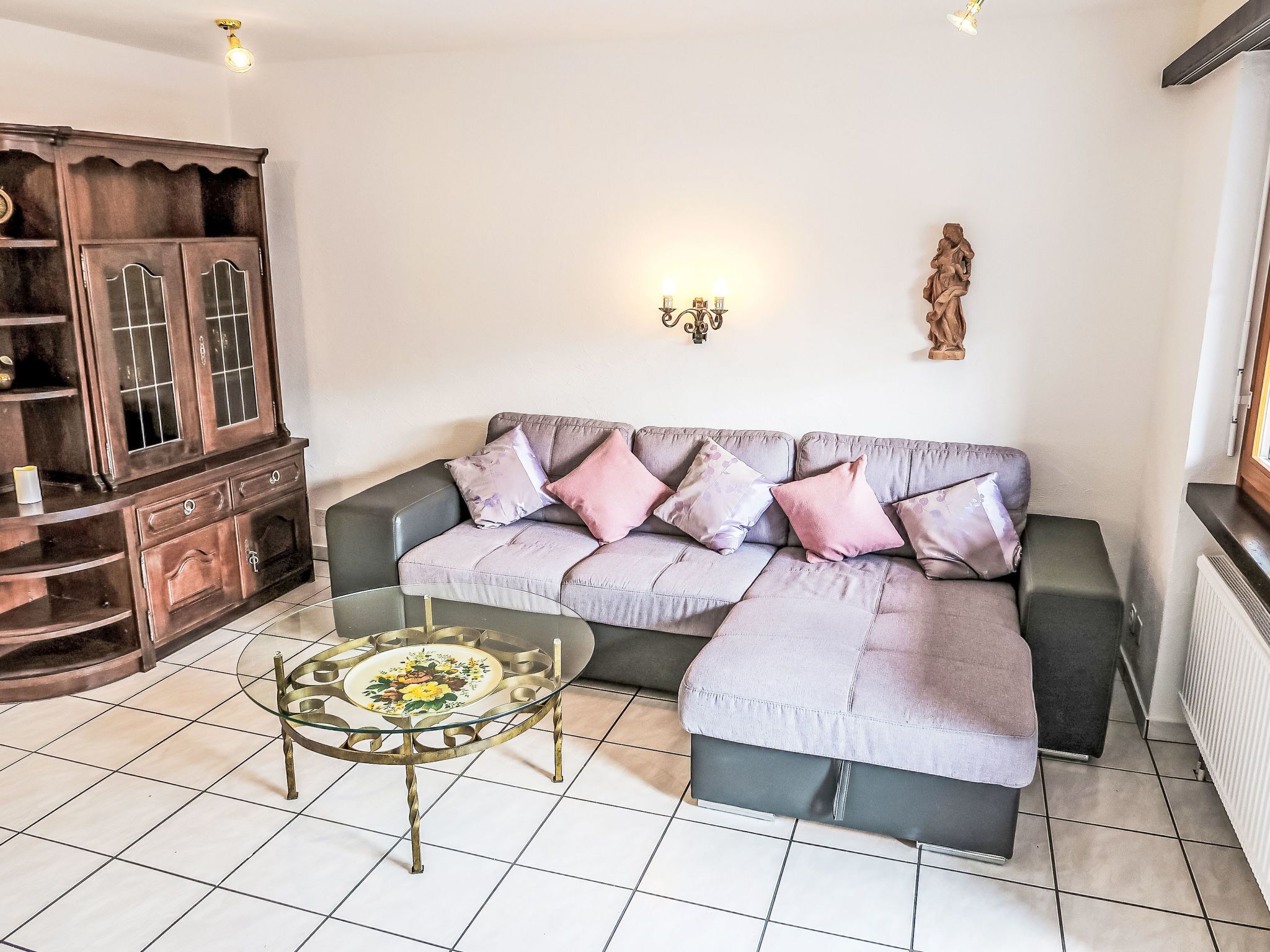 Ein Wohnzimmer mit einem Ecksofa, einem Glastisch und einer Holzkommode.