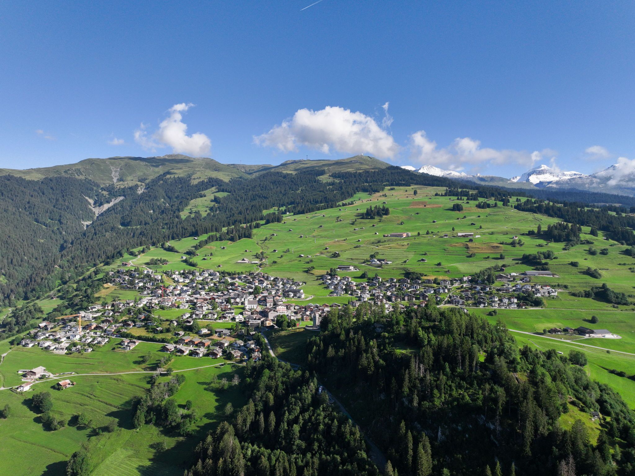 A small town nestled in a valley with green fields and forested hills in the background.