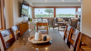 A dining area with a wooden table, chairs, and a view of the outdoors. - Seaside Oceanfront on the Prom | 5BR, Sweeping Views, and Direct Access to the Seaside Promenade (Seaside)