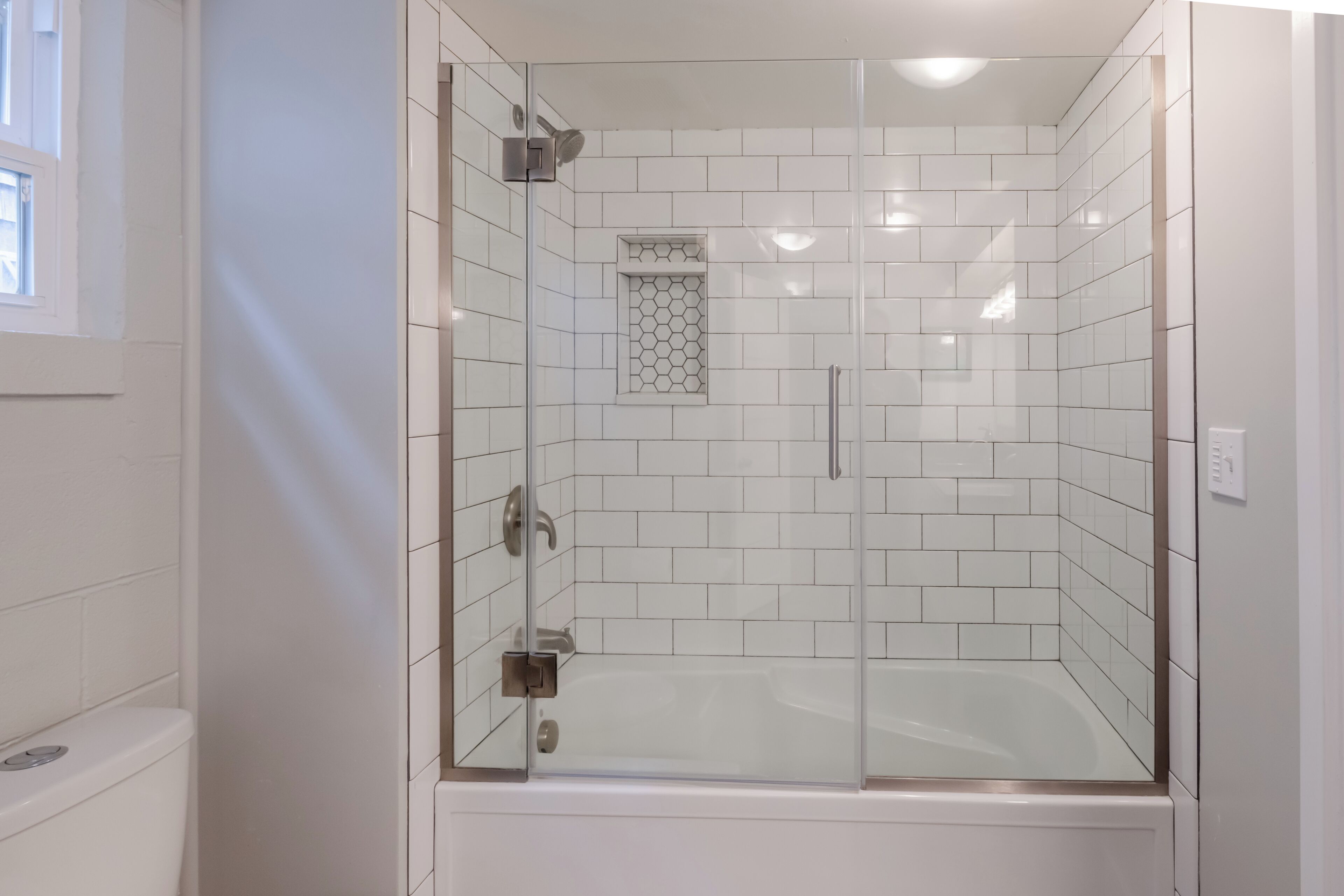 Un baño moderno con ducha de vidrio, paredes de azulejos blancos y un inodoro a la vista.