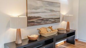 A modern living room with a black entertainment unit, two wooden lamps, a painting, and a wooden bowl. - Seaside Oceanfront on the Prom | 5BR, Sweeping Views, and Direct Access to the Seaside Promenade (Seaside)