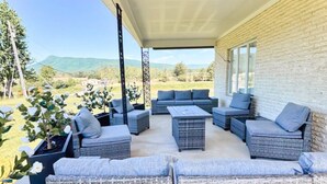 Uma área de estar coberta ao ar livre, com móveis de vime e vista para o campo.