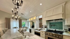 A modern kitchen with marble countertops, a gas stove, stainless steel appliances, and a chandelier. - Sea Glass Cottage North End Of Anna Maria• 2bed/2 bath w/ pool Steps to Beach (Anna Maria)