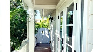 A covered porch with a wooden floor leading to a white door, surrounded by white railings and a white fence. - Sea Glass Cottage North End Of Anna Maria• 2bed/2 bath w/ pool Steps to Beach (Anna Maria)