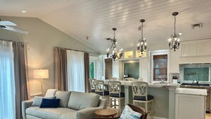 A modern living room with a sofa, chairs, a dining table, and a kitchen area with a stove and cabinets. - Sea Glass Cottage North End Of Anna Maria• 2bed/2 bath w/ pool Steps to Beach (Anna Maria)