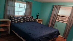 Ein Schlafzimmer mit einem Bett, einem Nachttisch, einem Schreibtisch und einem Fenster mit Vorhängen.