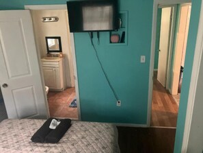 A bedroom with a bed, a television mounted on the wall, and a bathroom visible through an open door. - GPL Fort Myers Getaway (2670) (Fort Myers)