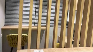 Une pièce avec une cloison en bois, une fenêtre avec des stores horizontaux et une chaise dotée d’un coussin texturé.