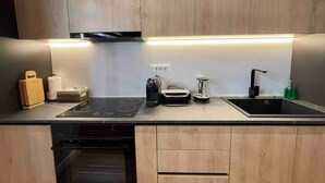Une cuisine moderne avec des meubles en bois, une cuisinière noire, un évier et un plan de travail sur lequel sont disposés divers appareils électroménagers.