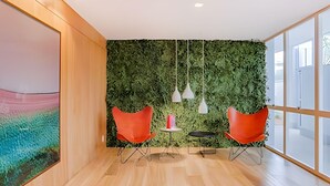 Ein moderner Arbeitsraum mit Holzboden, zwei roten Stühlen, einem kleinen Tisch mit einem roten Gegenstand und einer grünen Wand mit hängenden Lampen.