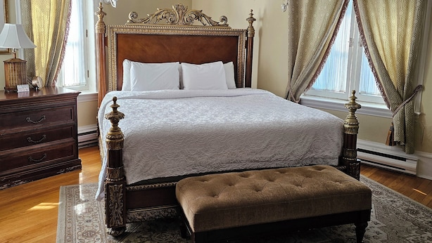 Une chambre à coucher classique, avec un grand lit, un banc en bois, une table de chevet et un tapis à motifs.