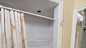 Une salle de bain aux murs recouverts de carreaux blancs, une douche avec une porte en verre et une serviette blanche sur le sol.