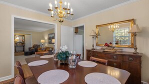 Un coin repas comprenant une table en bois, des sets de table, des chaises, un lustre, un miroir et une commode.
