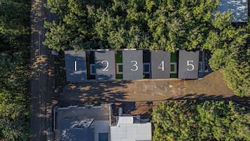 An aerial view of a row of numbered containers, likely temporary housing units, surrounded by trees and adjacent to a building.