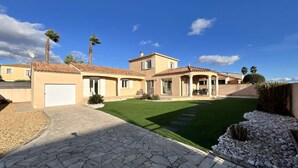 Uma casa em estilo mediterrâneo com telhado em telhas, varanda coberta e um gramado bem cuidado.