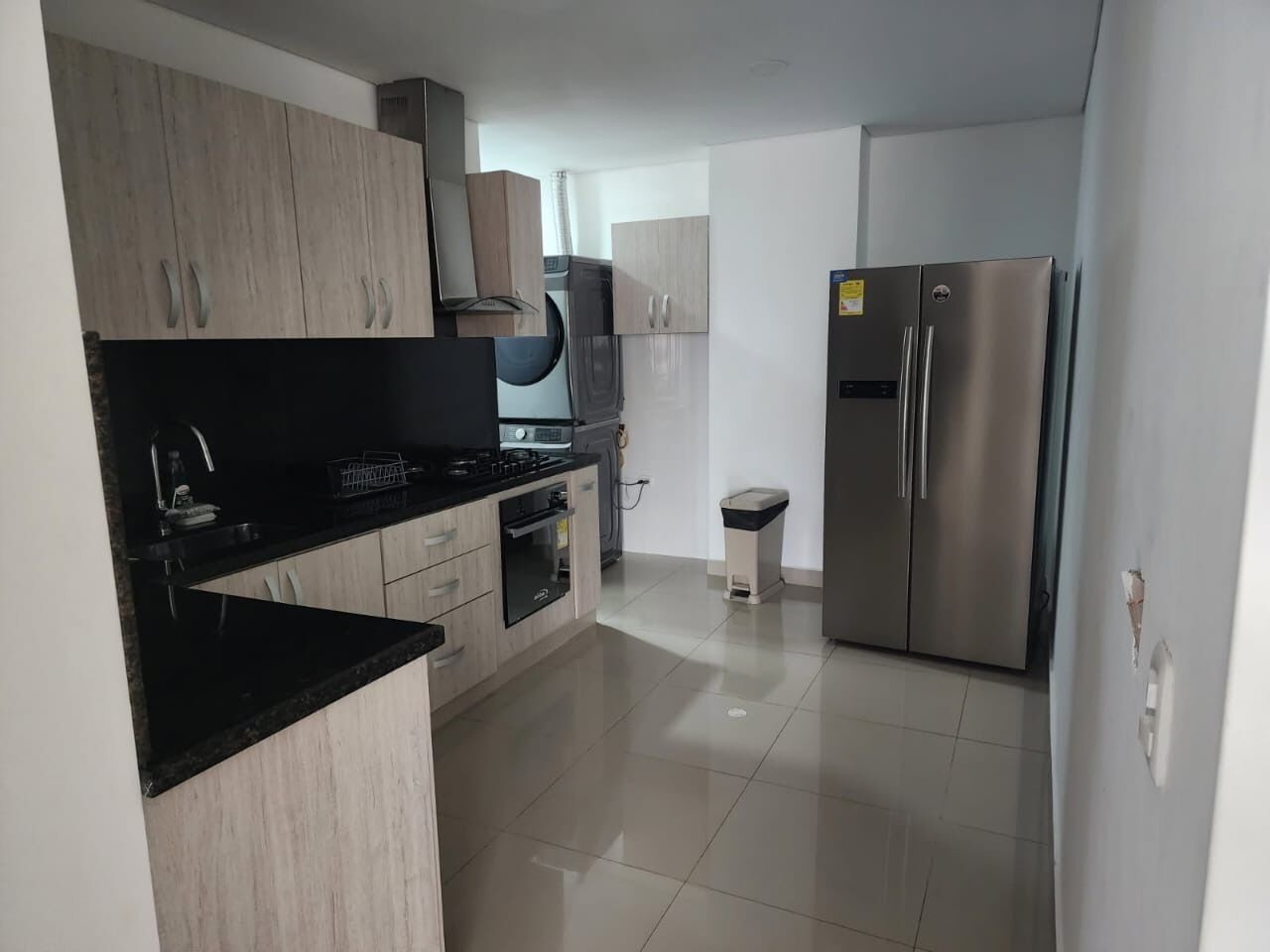 Una cocina moderna con alacenas de madera clara, encimera negra, electrodomésticos de acero inoxidable y piso de baldosas.