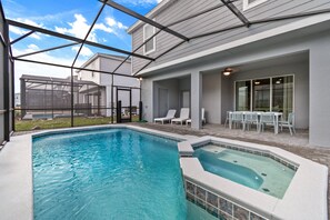 A swimming pool with a hot tub, surrounded by a covered patio area with chairs and a table. - 2207LC- Spacious 7-bedroom home in Davenport, perfect for large groups near attractions! (Davenport)
