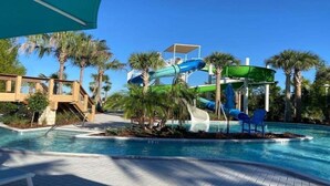 Ein Swimmingpool mit Wasserrutsche, Palmen und einer Holzterrasse.
