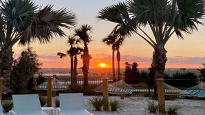 Strandszene mit Palmen, Sonnenuntergang und Liegestühlen.