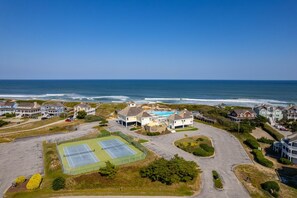 Ett bostadsområde vid kusten med hus, en tennisbana och utsikt över havet.