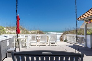 Eine Terrasse direkt am Strand mit weißen Stühlen und einer Schaukel, mit Blick auf den Ozean.