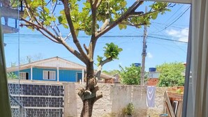 On aperçoit, à travers une porte vitrée, un jardin avec un arbre, un sol recouvert de gravier, un mur de briques et une maison en arrière-plan.