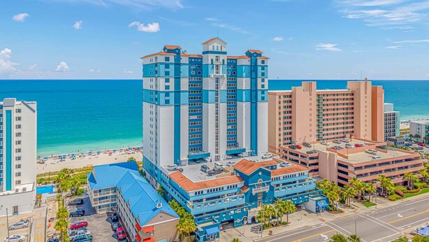 Un hotel frente al mar con varias construcciones, una playa y un cielo azul despejado.