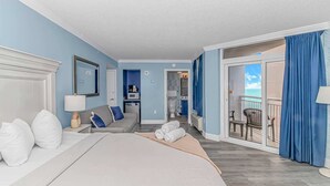 Habitación de hotel con cama, sofá, escritorio con lámpara, baño y balcón con vistas.