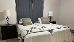 Una cama doble con colcha, dos mesitas de noche con lámparas, un tocador y una ventana con cortinas.