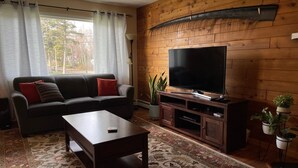 Una sala de estar con sofá, mesa de centro, televisor y plantas en macetas.