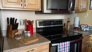 Una cocina con armarios de madera, un microondas de acero inoxidable, una estufa negra y un portalapices rojo.