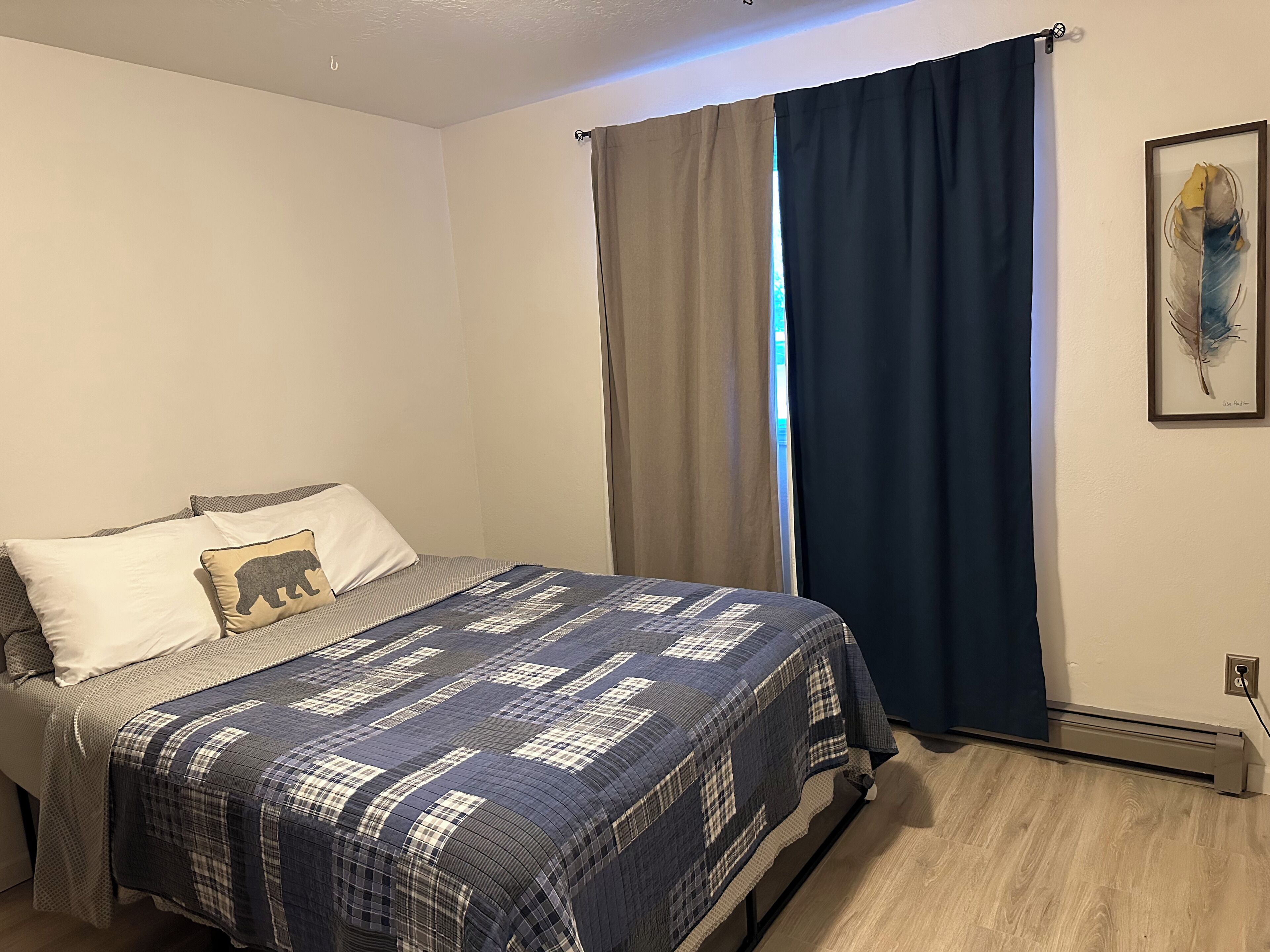 Un dormitorio con cama, ventana con cortinas y una obra de arte colgada en la pared.