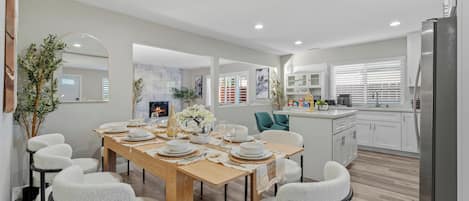 A modern kitchen with white cabinets, a stainless steel refrigerator, and a dining area with a wooden table and white chairs.