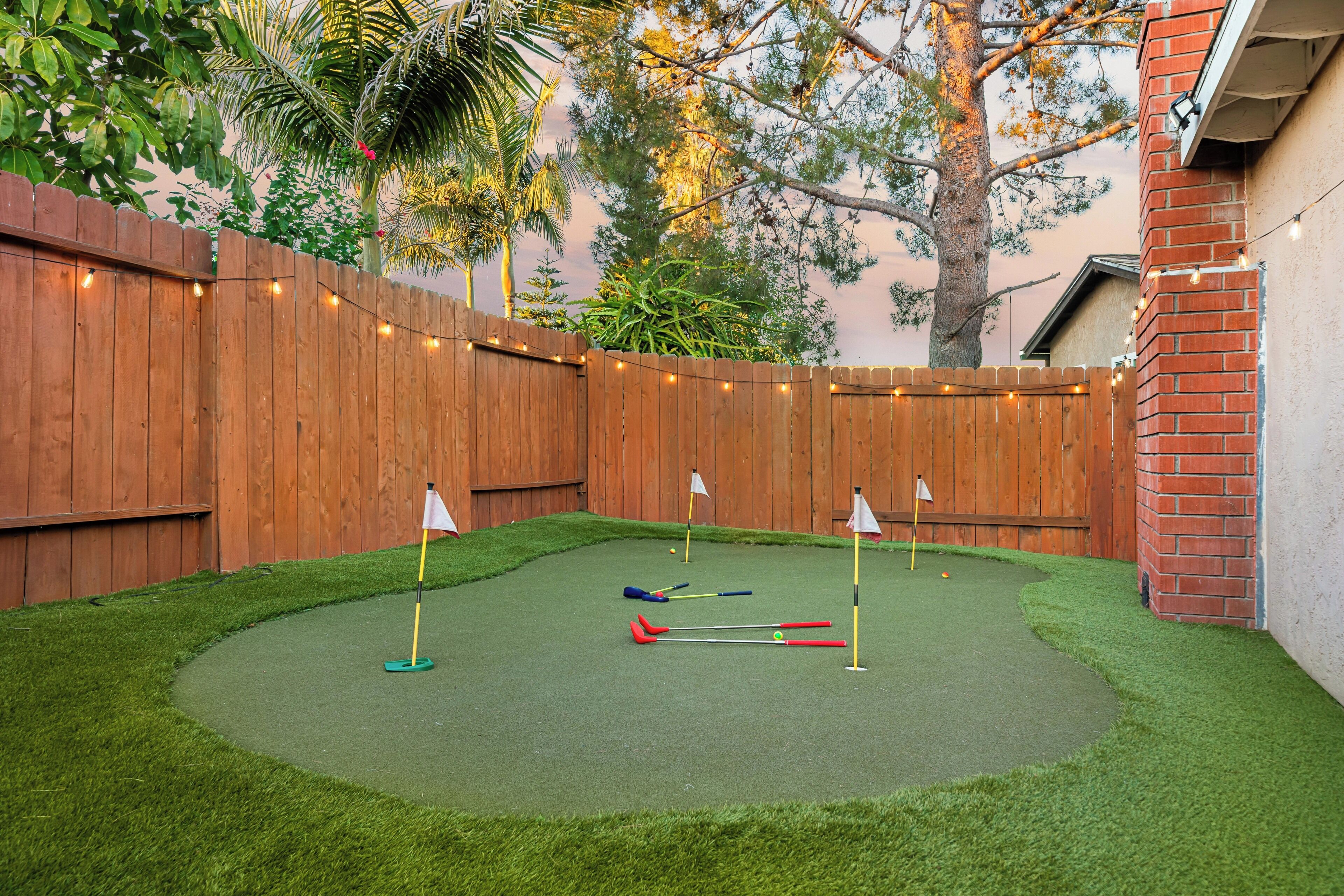 A backyard with a wooden fence, artificial grass, and a croquet set.