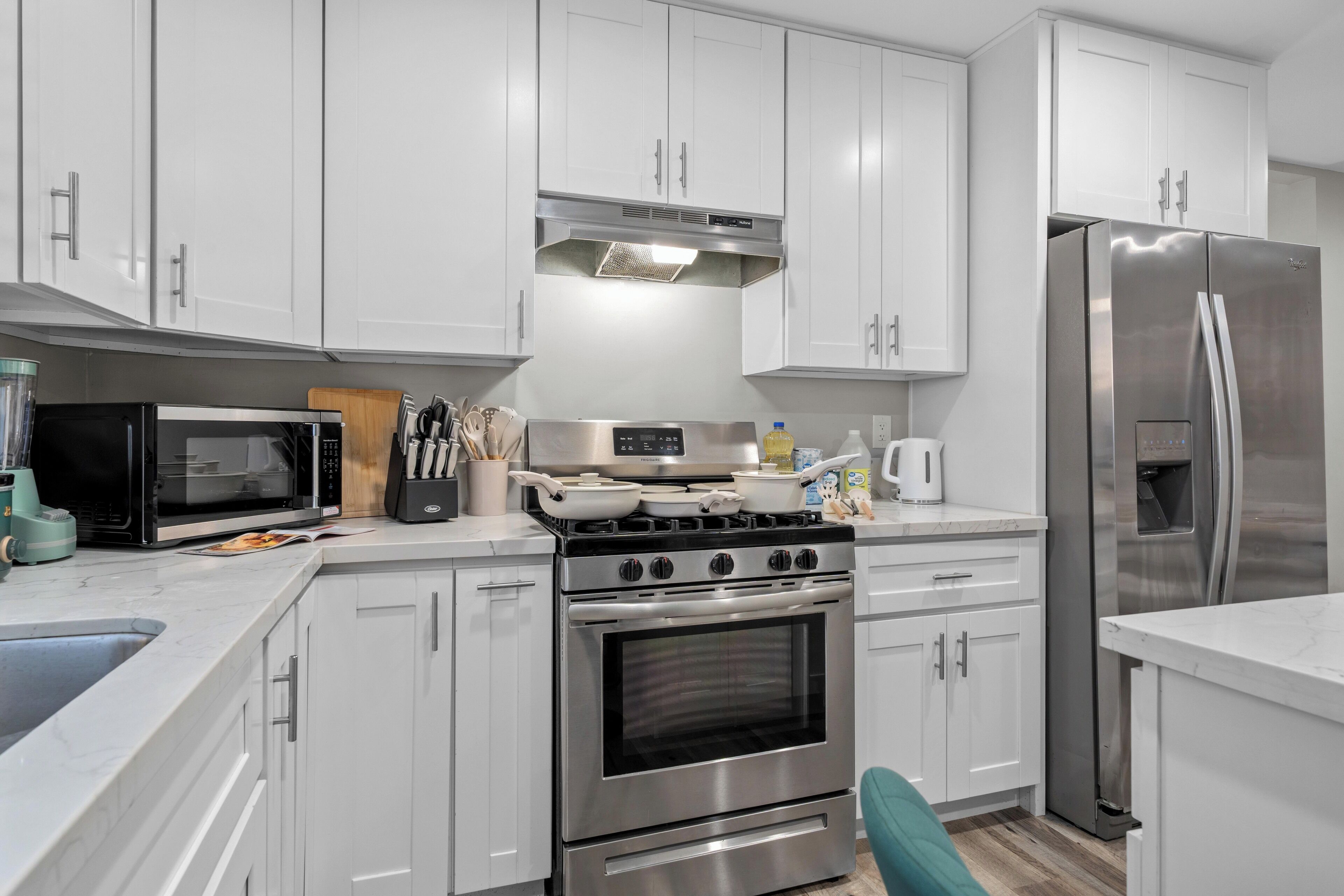 A modern kitchen with white cabinets, stainless steel appliances, and a teal chair.