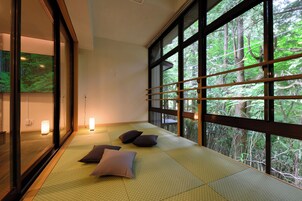 Un espacio con esteras de tatami y un amplio ventanal con vistas a un bosque.