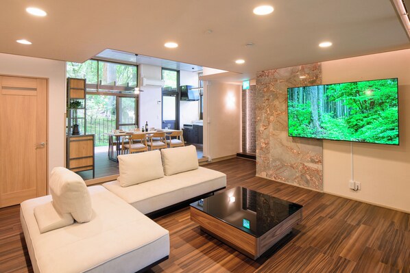 Una sala moderna con un sofá blanco, una mesa de centro de vidrio y un televisor de pantalla plana grande montado en la pared.