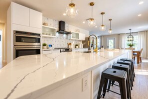 A modern kitchen with a marble countertop, built-in ovens, a stainless steel range hood, and pendant lighting. - Starfish Beach Vacation Villa by Golden Coast Rentals (Indian Rocks Beach)