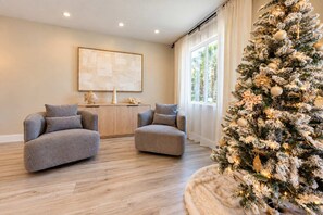 A modern living room with a large Christmas tree, two grey sofas, a wooden coffee table, and a large abstract painting on the wall. - Starfish Beach Vacation Villa by Golden Coast Rentals (Indian Rocks Beach)