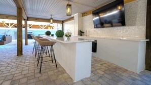 Moderni keittiö, jossa on suuri keittiösaareke, baarituolit, litteänäyttöinen televisio ja tiililattia.