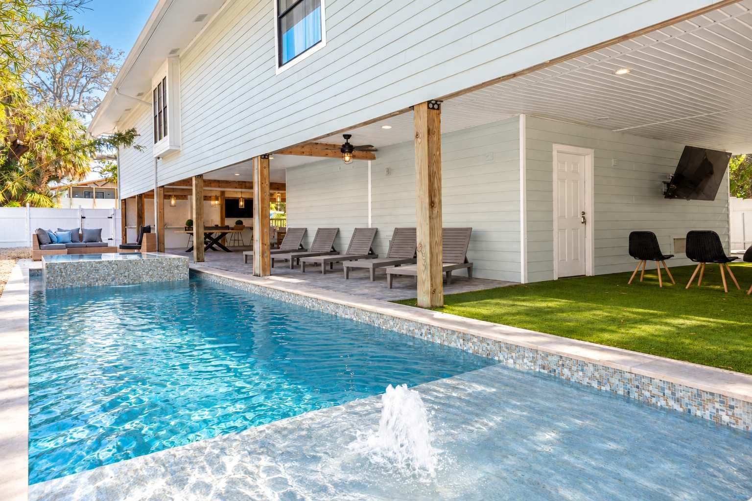 Une piscine avec un bord carrelé, des chaises longues et une zone herbeuse.