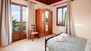 Een slaapkamer met een bed, een houten garderobe, een stoel en een balkon met gordijnen.
