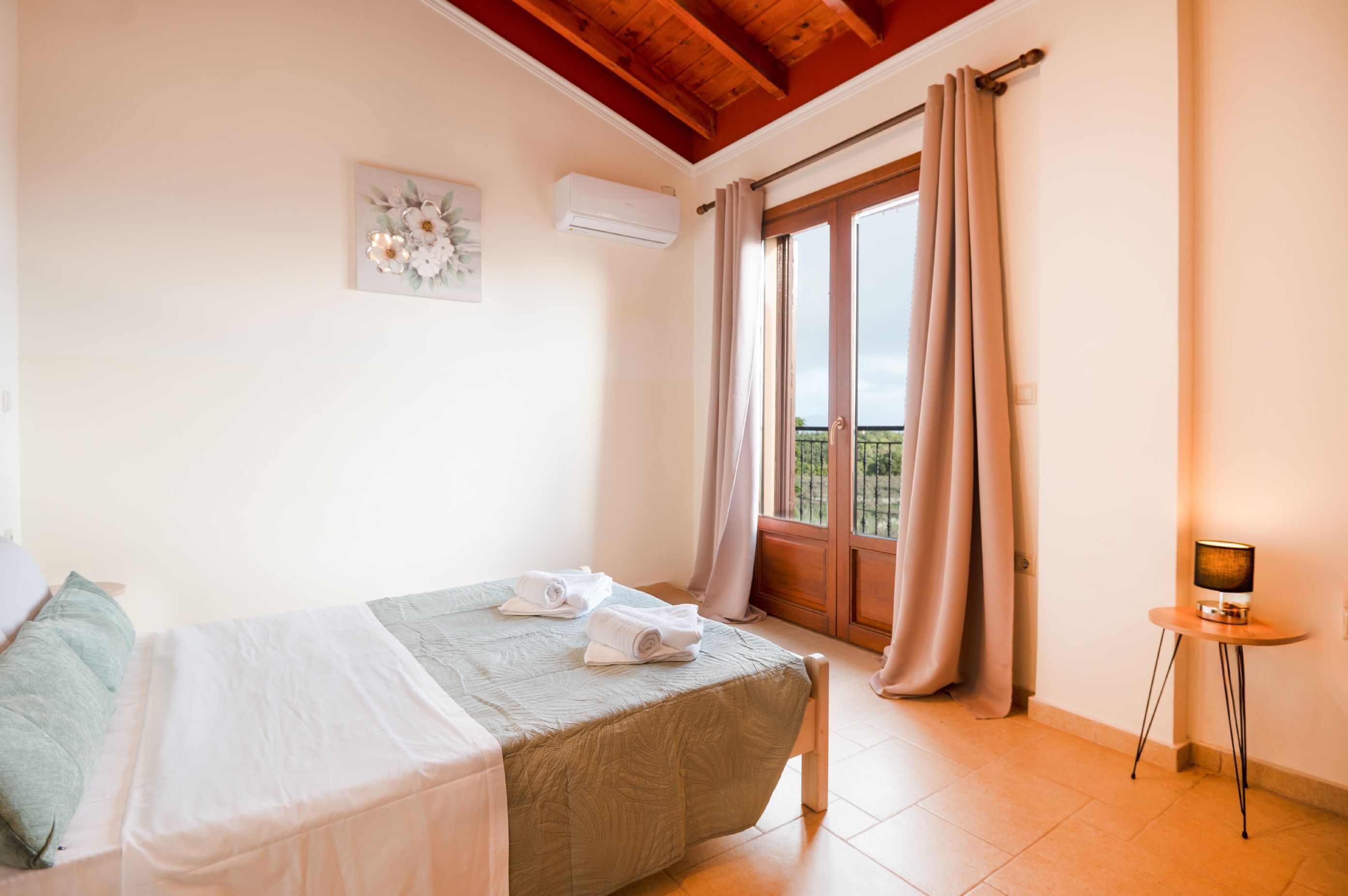 Une chambre à coucher avec un lit, une petite table avec une lampe, une fenêtre avec des rideaux et un climatiseur fixé au mur.