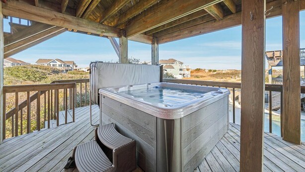 Ein Whirlpool auf einer Holzterrasse mit Blick auf Häuser und Strand im Hintergrund.