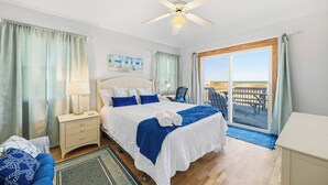 Ein Hotelzimmer mit Bett, Schreibtisch, Stuhl, Deckenventilator und Blick auf den Strand durch eine Schiebetür.