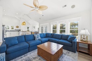 A spacious living room with a blue sectional sofa, a wooden coffee table, and a ceiling fan. - Tides Rollin' In | Private Pool, Hot Tub, & Fenced in Yard (Nags Head)